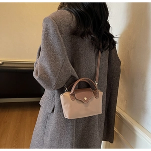 Detail of a minimalist two-tone leather crossbody bag with brown handle and metal snap