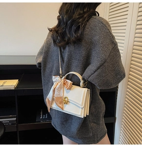 Detail of white leather handbag featuring gold clasp, silk scarf and thin shoulder strap