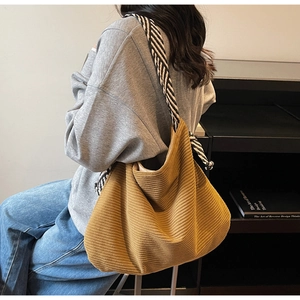 Detail of mustard yellow corduroy tote bag with black and white striped strap worn by model