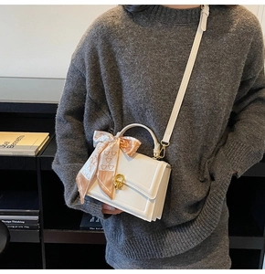 Detail of white leather crossbody bag featuring a golden twist lock and teddy bear scarf wrap