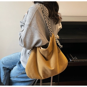 Detailed texture of mustard yellow corduroy tote bag with black and white striped strap