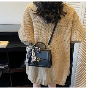 Close-up of black crossbody bag with gold twist lock and decorative scarf on handle