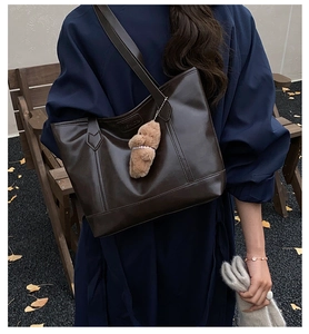 Detail of dark brown oil wax leather tote bag with fashion logo and teddy bear charm