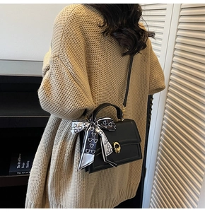 Detail of black crossbody bag with silk scarf on handle and golden twist lock closure