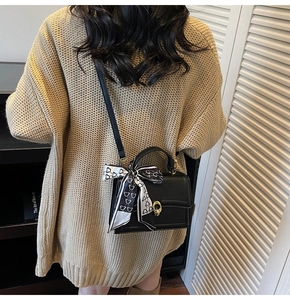 Detail of a black leather crossbody bag with a floral bear scarf and gold metal hardware