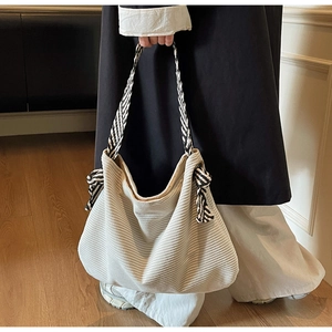 Detail of cream corduroy tote bag featuring black and white striped woven handle and side bows