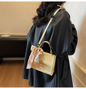 Detail of cream leather square handbag with golden twist lock and printed silk scarf handle
