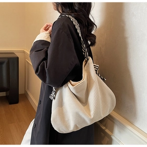 Close-up of beige corduroy tote bag with black and white striped woven shoulder strap