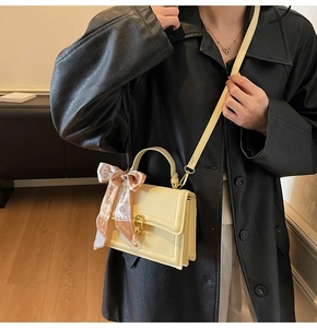 Close-up of cream crossbody bag with gold lock and decorative floral silk scarf on handle