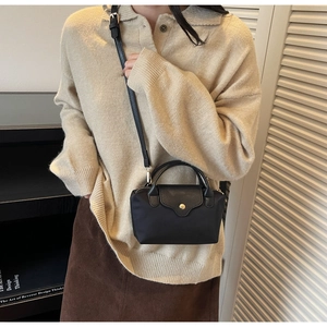 Detail of a black nylon crossbody bag with gold snap button worn by a model