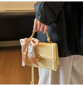 Detail of light yellow PU leather handbag with golden twist lock and printed silk scarf