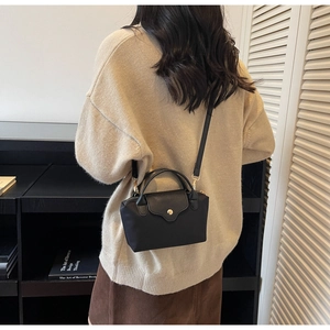 Detail of a black contrast minimalist handbag with gold metal clasp and leather handle