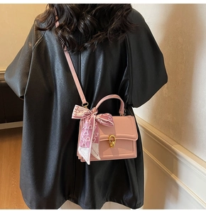 Detail of pink crossbody bag with golden twist lock and heart pattern scarf accessory