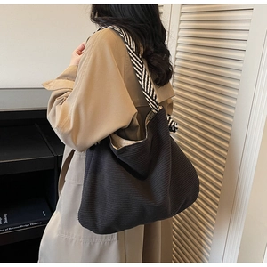 Detail of black corduroy hobo bag with striped strap worn over a khaki trench coat