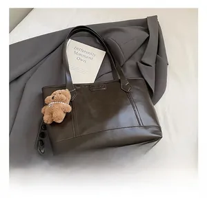Detail of deep brown tote bag featuring embossed FASHION logo and cute bear charm pendant