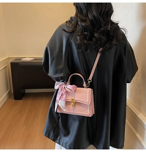 Detail of pink leather crossbody bag with gold twist lock and heart-patterned silk scarf