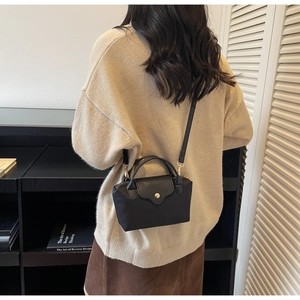 Detail of a black mini crossbody bag with a gold clasp worn by a model in a cozy sweater