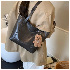 Detail of black leather tote bag with embossed logo and a cute brown plush bear charm