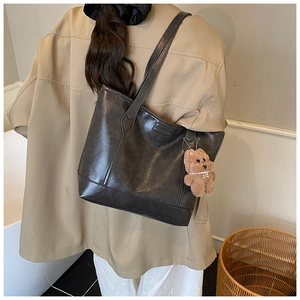 Detail of dark grey tote bag with fashion label and brown plush bear charm on shoulder