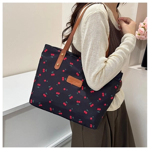 Close-up of a cherry print tote bag with brown leather handles worn by a model