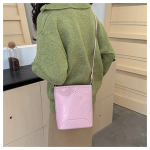 Gros plan d'un sac seau rose à motifs gaufrés porté sur un pull en maille vert