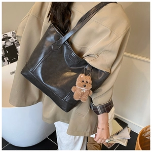 Detail of a black large tote bag with brown bear charm and soft leather texture