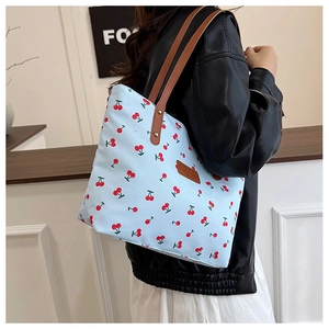 Light blue tote bag with cherry print and brown leather straps shown on a model