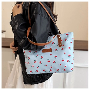 Detail of light blue cherry print tote bag with brown leather straps on a fashion model