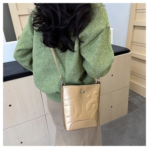Détail d'un sac seau vintage doré avec motifs gaufrés et fine bandoulière élégante
