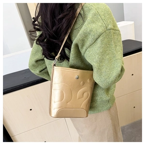Gros plan du sac seau doré avec gaufrage D2 et fini métallisé sur un pull vert