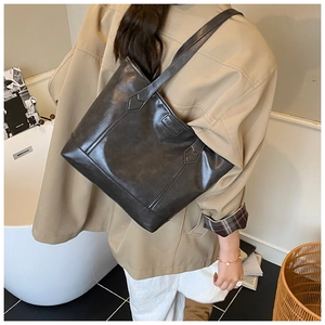 Detail of a large black faux leather tote bag with a fashion label worn by a model
