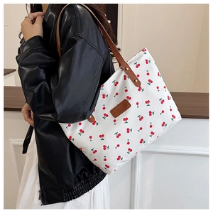 Detail of white tote bag featuring red cherry prints and brown leather handles