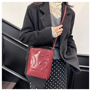 Détail du sac seau bordeaux avec motifs embossés vintage et boucle en métal argenté