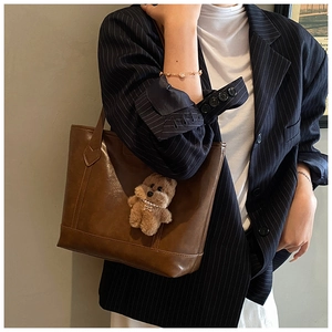 Brown leather tote bag with plush bear charm worn by a model in a navy striped blazer
