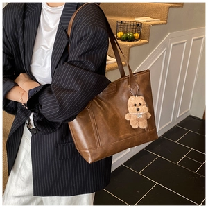 Detail of a brown leather tote bag with a fashion tag and a cute plush bear charm
