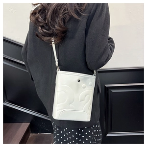 Détail du sac seau en cuir blanc montrant la texture gaufrée et le bouton pression argent