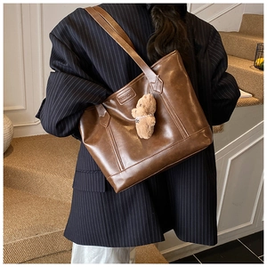 Detail view of brown faux leather tote bag with FASHION logo and plush bear charm