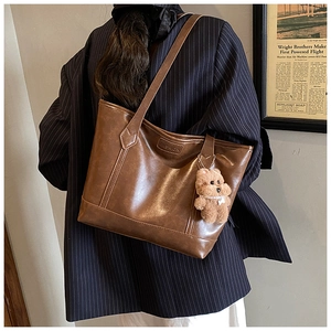 Rear view of a large brown leather tote bag with a fashion plaque and teddy bear charm