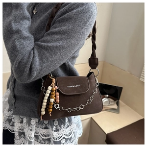 Detail of dark brown suede crossbody bag with floral metal chain and beaded charm
