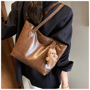 Detail view of large brown vintage tote bag with decorative stitching and bear charm
