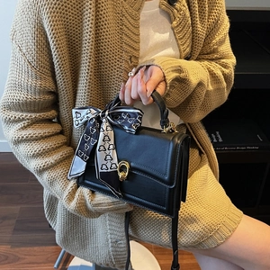 Classic black leather handbag with gold ring buckle and decorative polka dot silk scarf