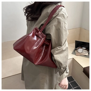 Detail of a dark red glossy pleated shoulder bag shown on model with aesthetic beige coat