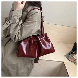 Detail of burgundy glossy pleated tote bag with drawstring closure on model shoulder