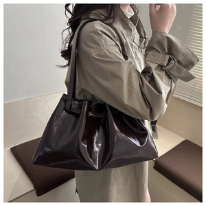 Detail einer dunkelbraunen Lackleder-Tote-Bag mit Seitenriemen auf beigem Trenchcoat