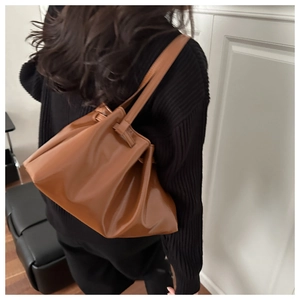 Brown pleated faux leather tote bag worn as a shoulder bag over a black sweater