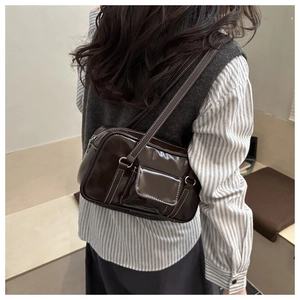 Detail of dark brown glossy PU leather shoulder bag with white contrast stitching