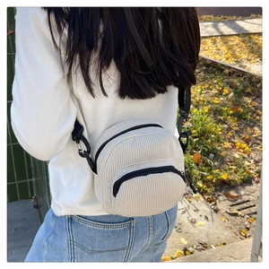 Close-up of cream corduroy crossbody bag featuring dual zippers and black adjustable strap