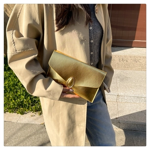 Détail de la pochette enveloppe dorée avec boucle ovale en métal et texture cuir
