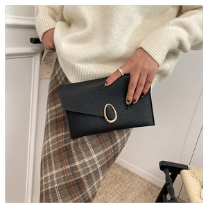 Détail d'une pochette noire en cuir texturé avec boucle dorée portée par un mannequin