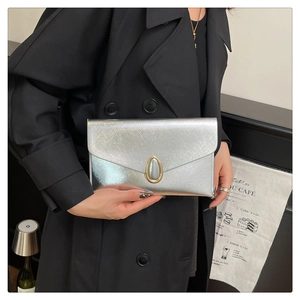 Détail de la pochette argentée brossée avec fermoir doré sur un trench-coat noir élégant